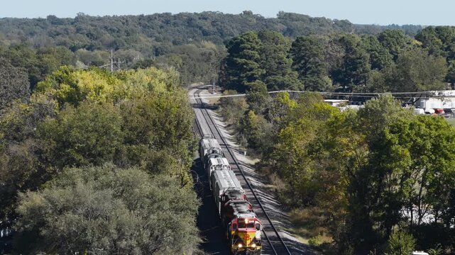 Freight locomotives traveling in a wooded railroad corridor in Gentry, Arkansas, aerial tilt down as locomotive backs up
