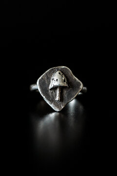 A silver ring with a mushroom design on a dark background. The ring features a unique leaf shape, highlighting the intricate details of the mushroom.