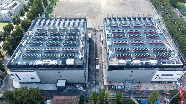 Aerial view of the Data 4 DC 11 data center construction site, featuring two large industrial buildings with rooftop cooling units, surrounded by trees in Castelletto, Lombardia, Italy.