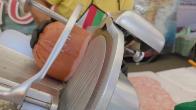 Wide view of deli meat being sliced with fresh slices laid out on paper