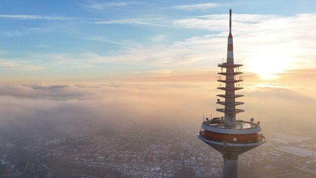 Aerial view of the Europaturm telecommunications tower rising above a thick layer of clouds during a golden sunset in Frankfurt am Main, Hessen, Germany.