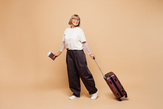 Traveler elderly woman wear casual clothes hold passport ticket bag isolated on plain pastel beige background studio. Tourist travel abroad in free time rest getaway. Air flight trip journey concept.