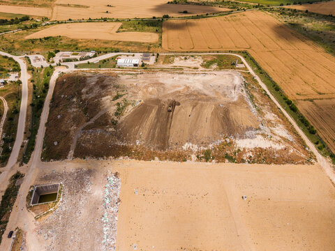 Aerial view of a landfill site with a bulldozer working on a mound of waste, surrounded by agricultural fields and roads in Varna, Varna, Bulgaria.