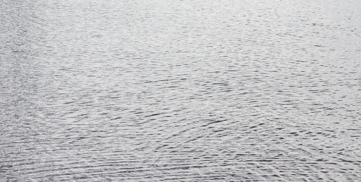 Calm water surface with light ripples and neutral grey tone background