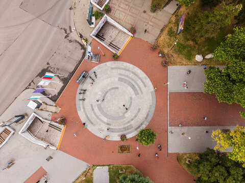 Aerial view of a circular paved plaza in the city center with pedestrians walking, surrounding trees, and stairs leading to an underground passage in Varna, Varna, Bulgaria.
