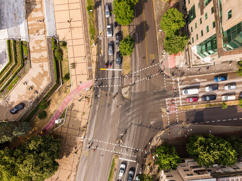 Aerial view of a busy city intersection with cars driving on asphalt roads, pedestrian crosswalks, surrounding buildings, and lush green trees in Varna, Varna, Bulgaria.