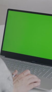 Close-up of female hand using laptop with chroma key green screen indoors at desk. Modern technology and professional software concept.