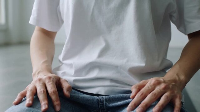 Breathing man making subtle wrist and finger moves in bright room, white tee blue jeans