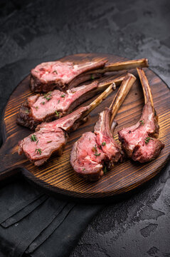 French roast lamb chops, mutton meat steaks on wooden board. black background. top view