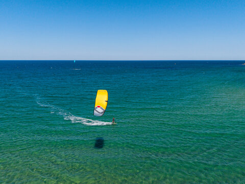 Aerial view of a kitesurfer gliding across the turquoise sea with a bright yellow kite under a clear blue sky in Lozenets, Burgas, Bulgaria.