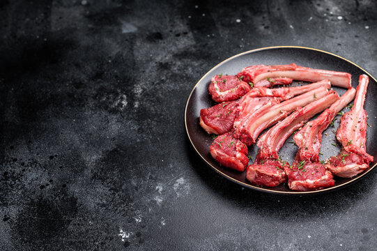 Fresh mutton chops, raw lamb meat cutlets on a plate. black background. top view