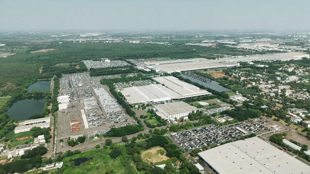 Aerial view of a car manufacturing unit with extensive parking lots filled with new vehicles, industrial buildings, and surrounding greenery in India.