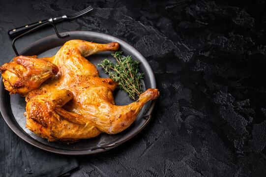 Roasted chicken Tabaka with herbs and spices, poultry meat on steel tray. black background. top view