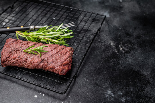 Grilled Flank steak, beef meat on rack with rosemary. black background. top view