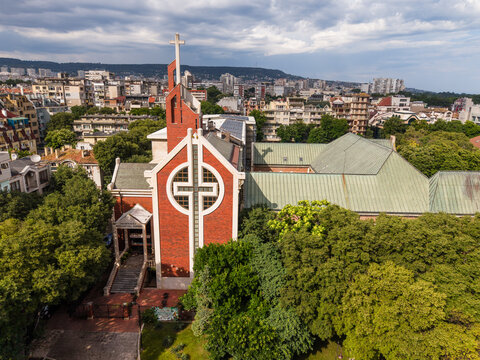 Aerial view of the Evangelical Methodist Episcopal Church with its distinctive red brick facade and cross-shaped window surrounded by lush green trees in Varna, Varna, Bulgaria.