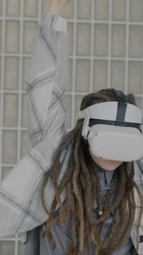 Slow motion of girl with dreadlocks having fun with augmented reality glasses dancing enjoying virtual party indoors. Entertainment and people concept.