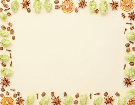 Charming decorative frame made from natural elements including fresh green hops, fragrant star anise, coffee beans, dried orange slices, and whole cloves on a light background