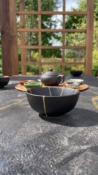 camera slowly reveals an outdoor tea ceremony setting with a black kintsugi-style bowl, clay teapot and colorful cups, highlighting mindful ritual, handcrafted pottery and slow living