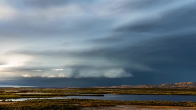 Storm clouds shift above reflective wetland channels and distant rugged hills in a remote wilderness. Nature documentaries, weather programming, and climate education.