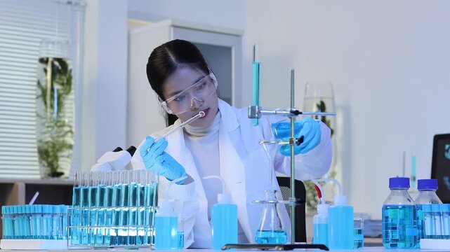 Asian scientist using a glass pipette and flask in a laboratory to conduct a chemical titration experiment for medical research, pharmaceutical development, or biotechnology