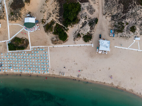 Aerial view of Atliman Beach featuring rows of blue umbrellas, wooden walkways, and small structures along the sandy coastline with turquoise water in Kiten, Burgas, Bulgaria.
