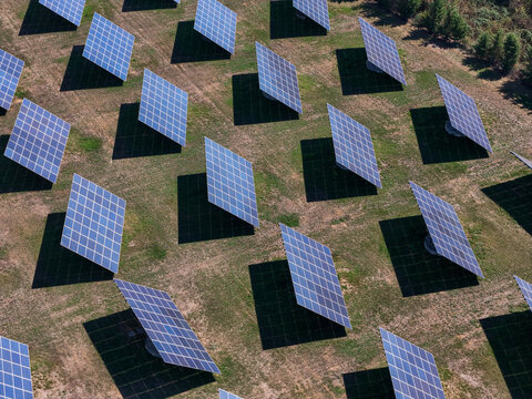 Aerial view of a solar panel system installed in a field with rows of photovoltaic panels casting long shadows on the grass in Spinetta Marengo, Piedmont, Italy.