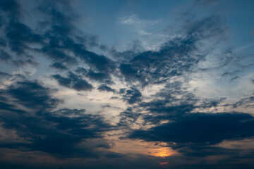 Fototapeta premium A horizontal sunset sky with dark blue-grey clouds and a warm orange glow breaking through at the bottom right. Moody atmosphere with dramatic cloud layers and copy space.