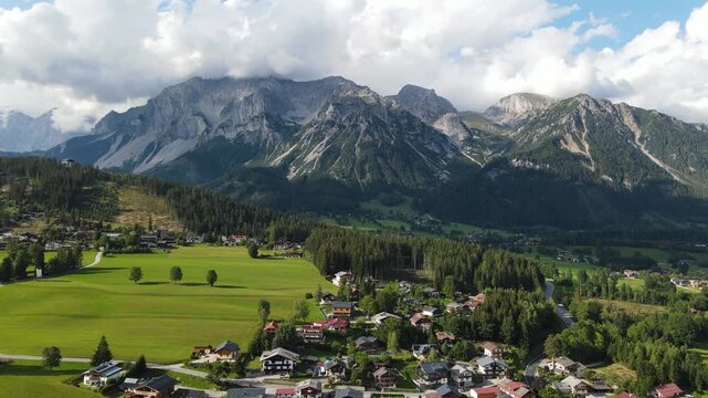 Aerial drone view of the Dachstein mountain near Ramsau am Dachstein in Austria. Slow flight over green alpine meadows, traditional mountain houses and forests in warm summer sunset light.