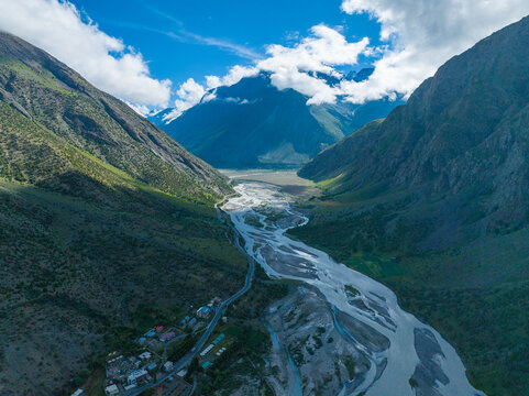 Aerial view of the winding river flowing through the rugged mountain valley of Ladakh with scattered buildings and lush green slopes in Ladakh Division, Ladakh, India.