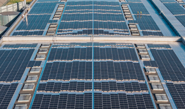 Aerial view of workers inspecting a large solar panel installation on an industrial warehouse rooftop, showcasing renewable energy infrastructure in Valence, Auvergne-Rhone-Alpes, France.