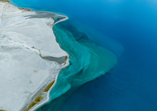 Aerial view of the turquoise waters of a high altitude lake meeting the white sandy shores in Ladakh Division, Ladakh, India.