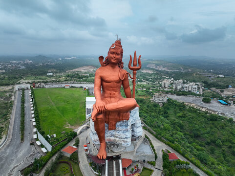 Aerial view of the massive Statue of Belief, a towering copper-colored Shiva statue holding a trident, set amidst lush green landscapes and winding roads in Nathdwara, Rajasthan, India.