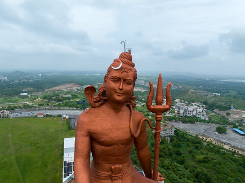 Aerial view of the massive Statue of Belief, a towering bronze-colored depiction of Lord Shiva holding a trident, set against a lush green landscape in Nathdwara, Rajasthan, India.