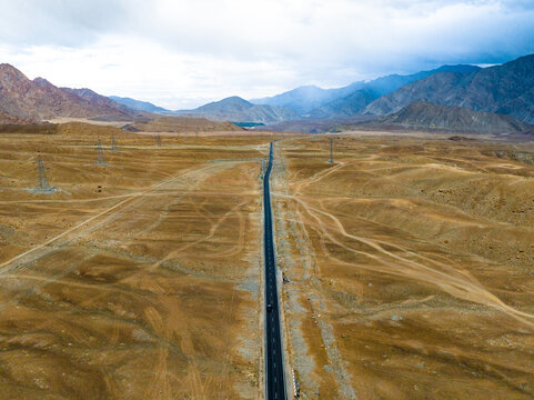 Aerial view of a long straight road stretching through the arid mountainous landscape of Ladakh with power lines and vast desert terrain in Ladakh Division, Ladakh, India.