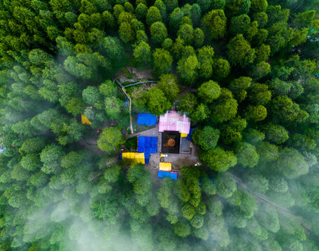 Aerial view of the historic Hidimba Devi Temple nestled within a dense cedar forest, featuring its distinctive pagoda-style roof and surrounding colorful tarps in Manali, Himachal Pradesh, India.