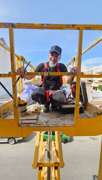 Real senior professional painter aged 63&ndash;66 working on a residential building from an elevated platform