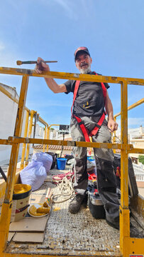 Real senior professional painter aged 63&ndash;66 working on a residential building from an elevated platform