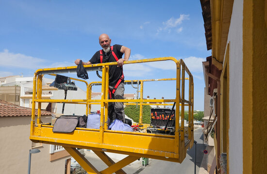 Real senior professional painter aged 63&ndash;66 working on a residential building from an elevated platform