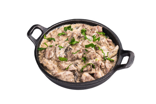 Creamy beef stroganoff with fresh greenery in a skillet isolated on white background. top view