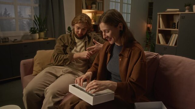 Young Caucasian woman unboxing digital tablet gift and hugging partner. Visual ideal for consumer electronics advertising and holiday promotional campaigns