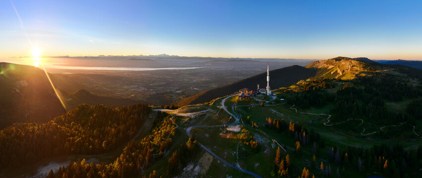 Aerial view of the sunrise over the High Jura mountain ridges featuring a communication tower, lush forests, and the valley landscape in Gex, Auvergne-Rhone-Alpes, France.
