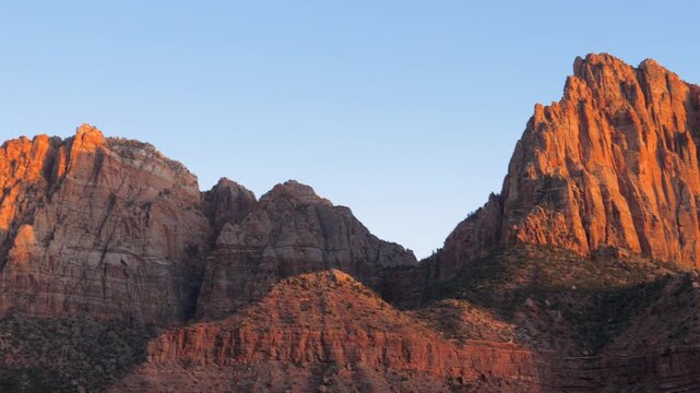 Majestic red rock mountains of zion national park in utah catching last warm red light of setting sun against a clear blue sky, highlighting the rugged sandstone cliffs and peaks