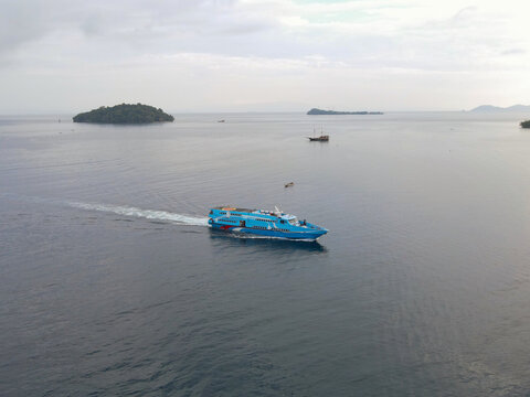 Aerial view of a blue passenger ferry boat cruising through the calm waters near Waisai Harbour in Raja Ampat, Papua Barat Daya, Indonesia.