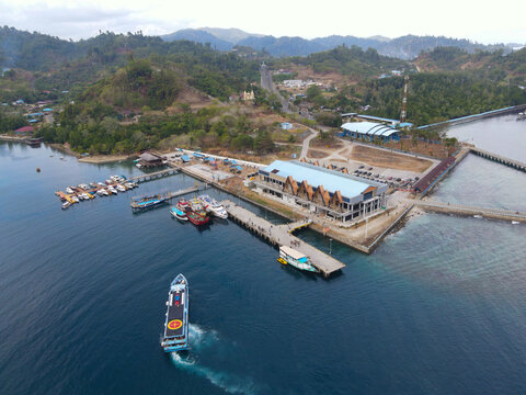 Aerial view of Waisai Harbour with boats docked at the pier, clear blue water, and lush green hills in the background in Raja Ampat, Papua Barat Daya, Indonesia.