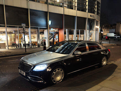 Luxury Mercedes Maybach parked on a London, UK street at night outside a coffee shop with illuminated city building