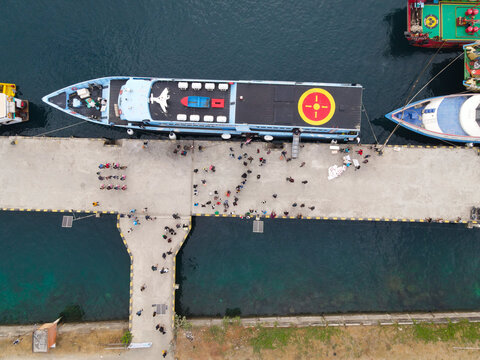 Aerial view of Waisai Harbour with a ferry docked at the concrete pier and people walking along the waterfront in Raja Ampat, Papua Barat Daya, Indonesia.