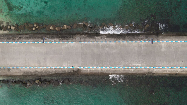 Aerial view of Waisai Harbour showing the concrete pier structure extending into the turquoise waters with rocky breakwaters and clear sea, Raja Ampat, Papua Barat Daya, Indonesia.