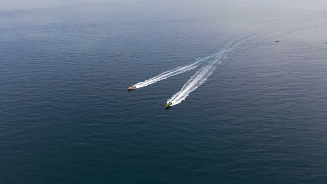 Aerial view of two speedboats traveling across the deep blue sea, leaving white wakes behind them in Raja Ampat, Papua Barat Daya, Indonesia.