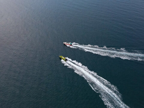 Aerial view of two speedboats traveling through the deep blue waters near Waisai Harbour, leaving white wakes behind them in Raja Ampat, Papua Barat Daya, Indonesia.