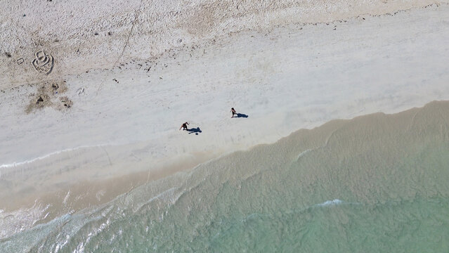 Aerial view of Tanjung Aan Beach with two people walking on the white sand near the turquoise water in Central Lombok Regency, West Nusa Tenggara, Indonesia.
